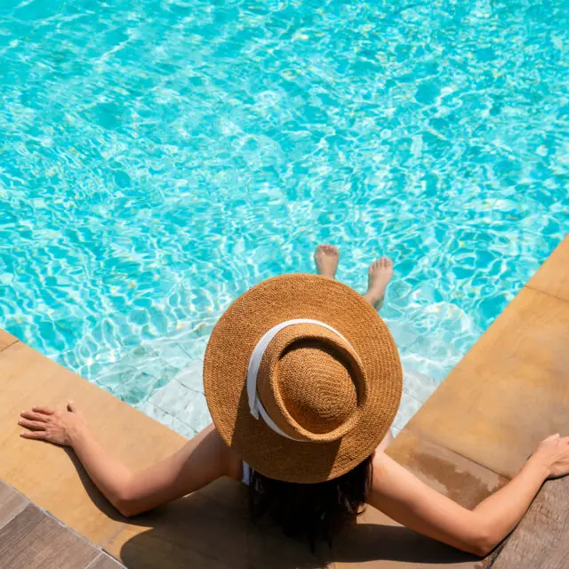 Top view of woman wear a hat sitting and relaxing in swimming pool, swimming pool scenery on background. Summer holidays, vacation, travel concept. Copy space